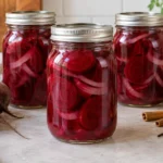 Three sealed pint canning jars filled with sliced pickled beets and onion