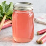 Jar of pale pink rhubarb juice with fresh rhubarb stalks