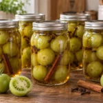 Six sealed pint jars of whole spiced green tomatoes with cinnamon and cloves.